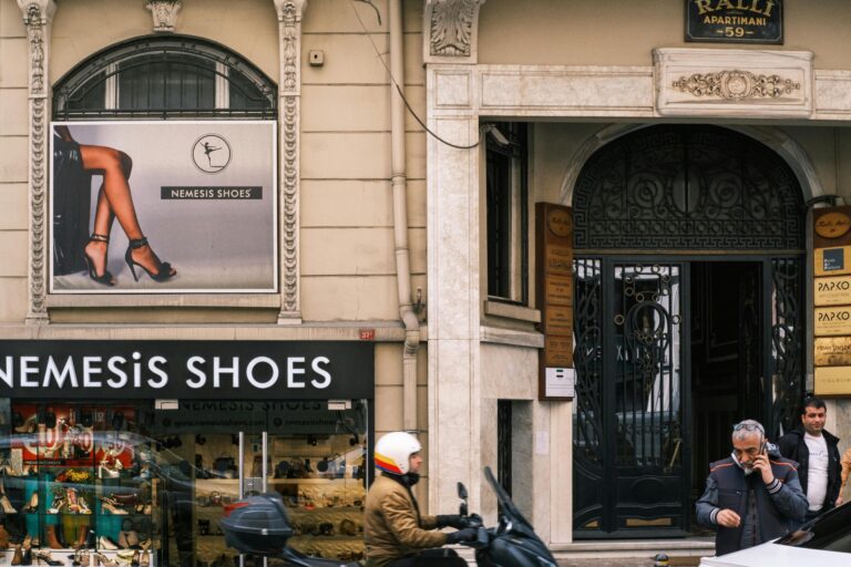 Urban street view with Nemesis Shoes boutique, pedestrians, and scooter, capturing daily city life.